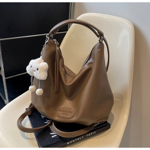 Détail du sac fourre-tout en cuir marron avec gland et charm nuage sur une chaise moderne
