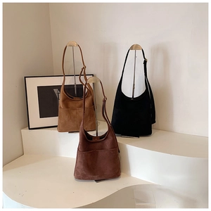 Three oversized suede tote bags in brown and black on minimalist display stands