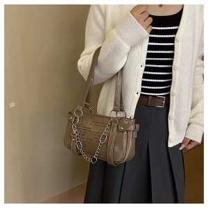 Brown leather crossbody bag with silver chain strap and metal buckle detail on model