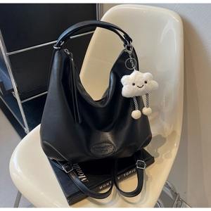 Détail du sac cabas en cuir mat noir sur chaise blanche avec breloque nuage blanc