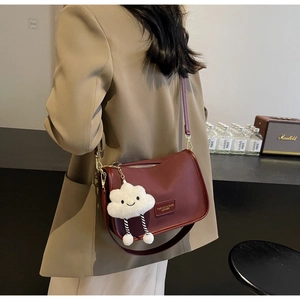 Detail of burgundy leather shoulder bag with plush charm and fashion brand label