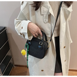 Détail d'un mini sac noir avec logo en relief et breloques porté sur un trench-coat beige