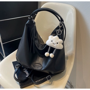 Détail du grand sac sous le bras noir avec breloque nuage en peluche sur chaise blanche