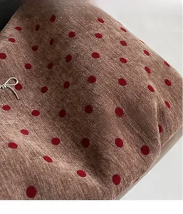 Close-up of red polka dots on brown fabric with a silver bow metal charm detail
