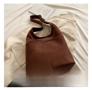 Detailed view of dark brown suede bucket bag with front pockets on soft fabric
