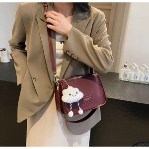 Detail of burgundy PU leather crossbody bag with fluffy white cloud charm and gold hardware