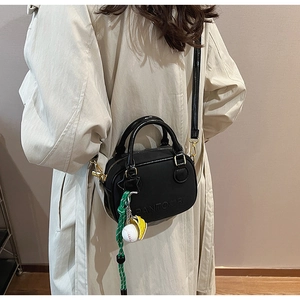 Detail of black mini crossbody bag with gold hardware and baseball charm on beige trench coat