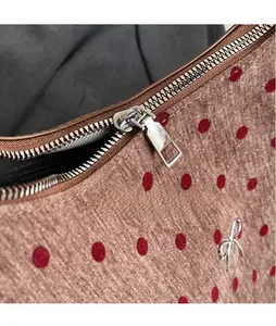 Close-up of brown polka dot fabric with silver metal zipper and decorative bow charm