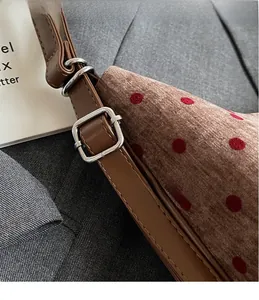 Close-up of brown polka dot shoulder bag with adjustable silver metal buckle detail