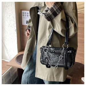 Street style shot of a black leather crossbody bag with silver chain and white lettering