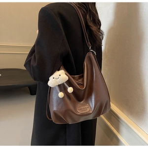 Détail du sac cabas en cuir marron foncé avec breloque nuage sur un manteau noir