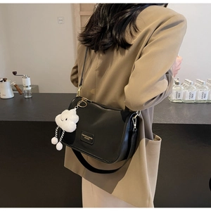 Detail of black leather crossbody bag with golden zipper and white plush cloud charm