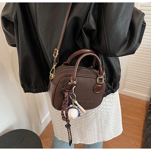 Detail of dark brown leather handbag with TOUR embossing and sporty baseball charm