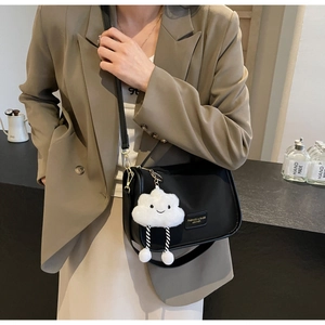Detail of black leather shoulder bag with a white cloud plush charm on a khaki blazer