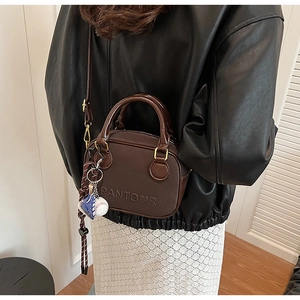 Détail du sac bandoulière en cuir marron foncé avec logo embossé et breloque baseball