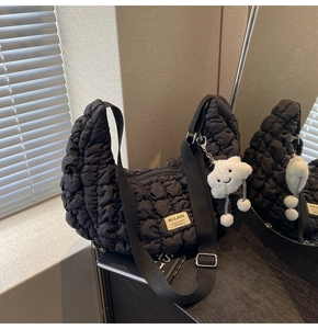 Détail du sac croissant noir matelassé avec un charm peluche et une étiquette
