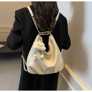 Détail d'un sac hobo en cuir beige avec breloque nuage porté sur un blazer noir