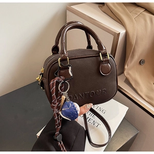 Detail of a dark brown mini handbag with a creative baseball charm on a matte PU surface
