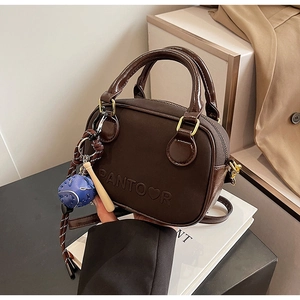 Close-up of a dark brown crossbody bag with heart embossing and a baseball charm detail