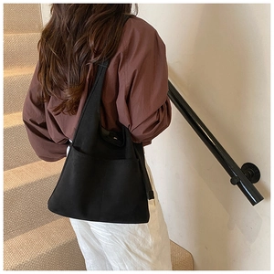 Detail view of large black canvas tote bag with front pockets on female model shoulder