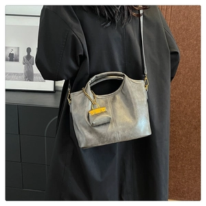 Detail of vintage grey leather crossbody bucket bag with yellow charm on black coat