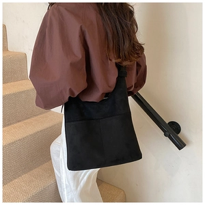 Detail view of the black suede tote bag texture and large front pocket on a shoulder bag
