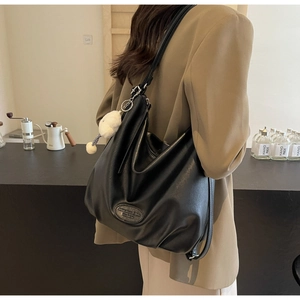 Détail d'un sac cabas en cuir noir avec bandoulière chaîne et porte-clés peluche
