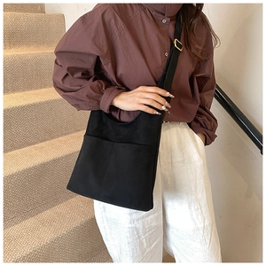 Detail of minimalist black fabric bucket bag with dual front pockets and gold buckle