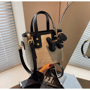 Close-up of retro bucket bag with black leather trim, gold rivets, and puppy charm