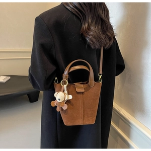 Detail view of brown suede bucket bag with leather handle and cartoon monkey charm