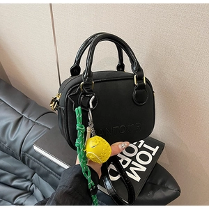 Détail du sac à main en cuir noir avec logo embossé et pendentif de baseball jaune