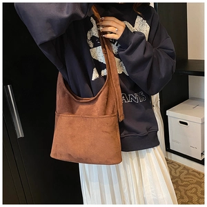 Detail of a brown suede crossbody bucket bag with visible stitching on the exterior pocket