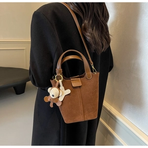 Detail of dark brown matte leather bucket bag with vertical stitching and bear charm