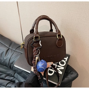 Détail d'un sac à main en cuir marron foncé avec logo, bandoulière et charms