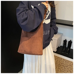 Close-up of brown suede shoulder bag with stitching details shown on a model
