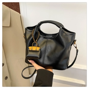 Detail of black leather tote bag featuring a decorative mini bag charm and shoulder strap