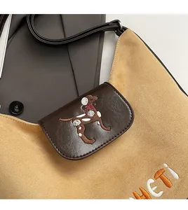 Dettaglio della borsa retrò in pelle scamosciata con ricamo 'HETI' e patch di cucciolo