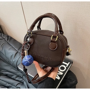 Détail du mini sac Boston marron foncé avec logo en relief et pendentif planète bleue