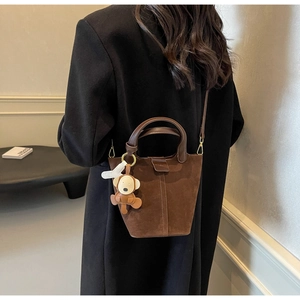 Brown suede bucket bag with shoulder strap and cartoon monkey pendant on black wool coat