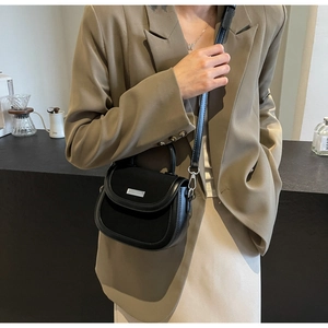 Détail du sac selle noir avec textures mixtes, boucle argentée et bandoulière amovible