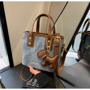 Close-up of blue denim tote bag with brown leather trim and cute puppy charm detail
