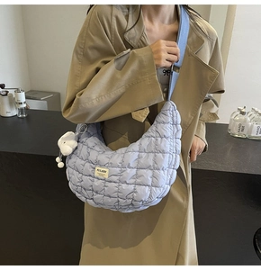 Détail du sac hobo matelassé bleu clair avec ourson porté sur un trench-coat chic