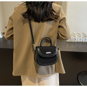 Détail du sac selle en cuir noir et toile avec boucle argentée et bandoulière réglable