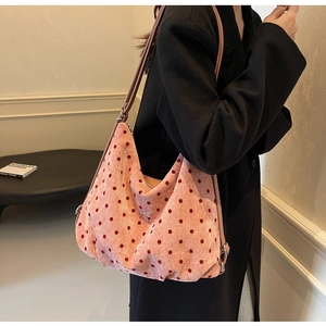 Detailed view of a pink polka dot tote bag with a small metal bow on a dark coat model