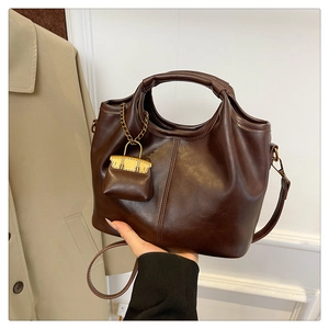 Detail of dark brown leather tote bag with a golden miniature handbag charm accessory