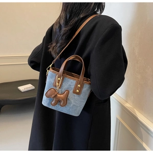 Detail of light blue denim mini bucket bag with brown leather trim and puppy charm