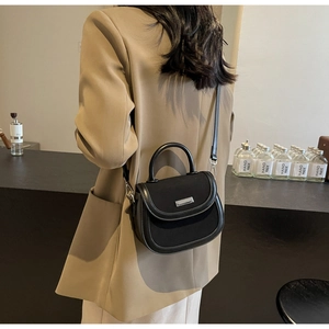 Mannequin portant un sac selle noir en cuir avec logo argenté et poignée supérieure chic