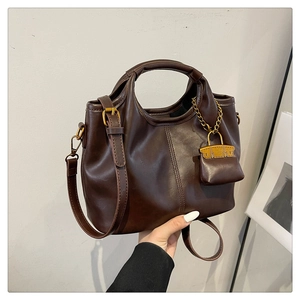 Detail view of brown PU leather handbag with gold mini bag charm and round handle