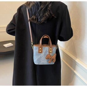 Detail of blue denim bucket bag with brown leather trim and a cute puppy charm