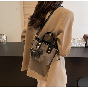 Detail of taupe bucket bag featuring stone texture, golden hardware and a dog charm